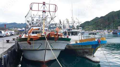Asian fishing boats anchored in port. Taiwanese multi-colored fishing trawler moored in bay on background of green mountains, Fishing industry in Asia. fishermen prepare gear