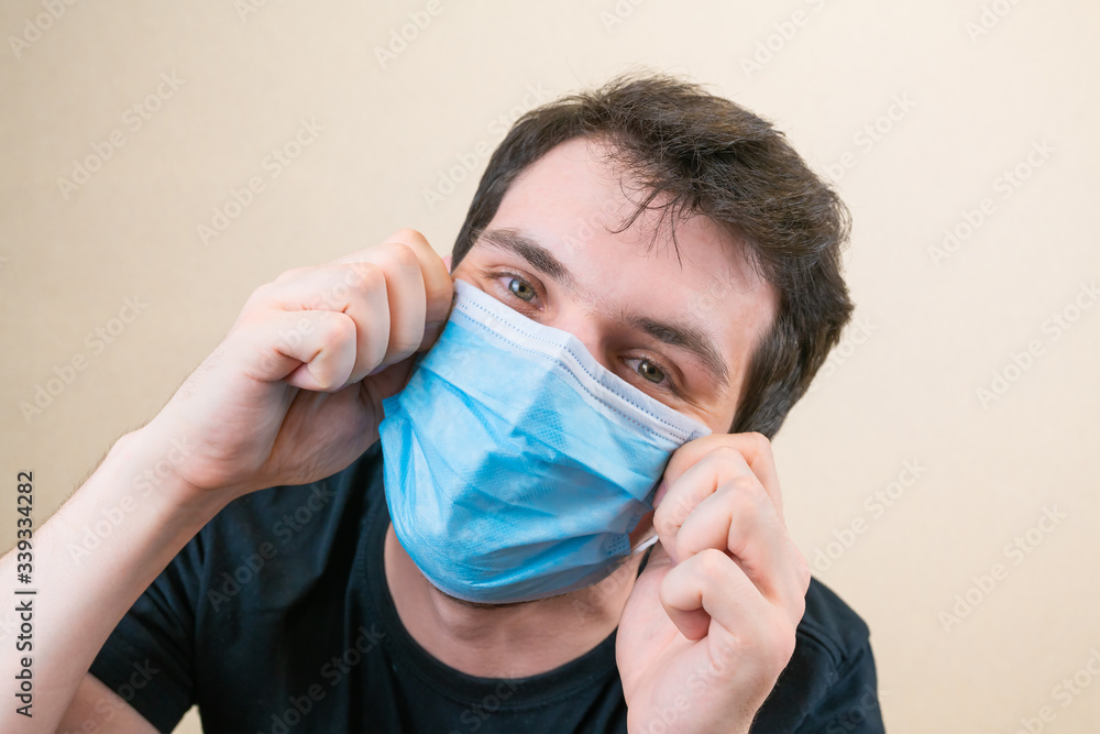 Young man in blue protective medical mask and happu with it. Self-isolation and quarantine. Stay home Young man in blue protective medical mask and happu with it. Self-isolation and quarantine. Stay home