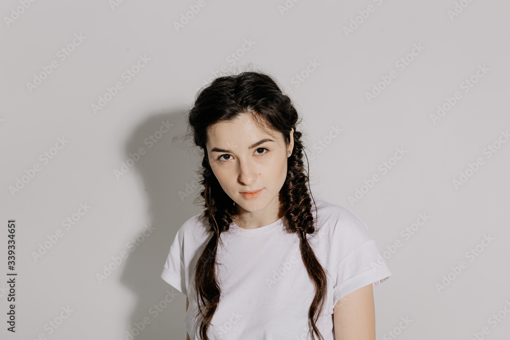 Young pretty woman with pigtail braid dressed in white t-shirt and jeans posing for photo on a white background in front of studio light Young pretty woman with pigtail braid dressed in white t-shirt and jeans posing for photo on a white background in front of studio light