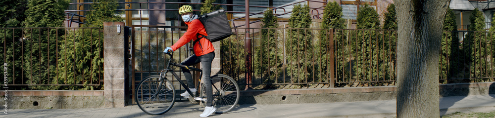 Delivery man courier wearing medical mask arrives at residential address to deliver food order to customers during virus outbreak. Coronavirus, COVID-19, safe delivery