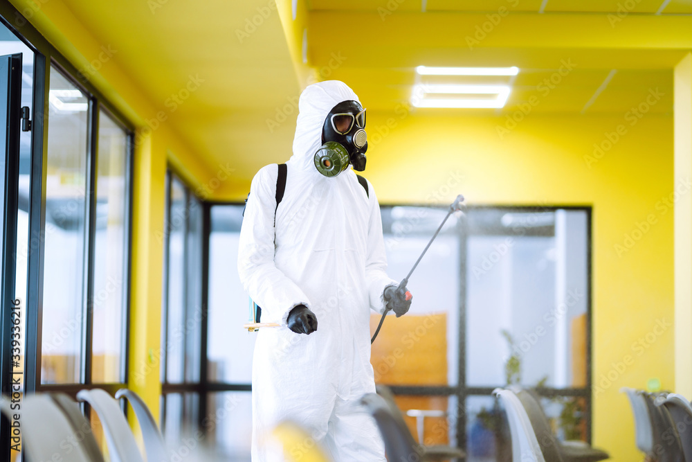 Man wearing protective suit disinfecting assembly hall with spray chemicals to preventing the spread of coronavirus, pandemic in quarantine city. Disinfecting of office. COVID-19. Man wearing protective suit disinfecting assembly hall with spray chemicals to preventing the spread of coronavirus, pandemic in quarantine city. Disinfecting of office. COVID-19.