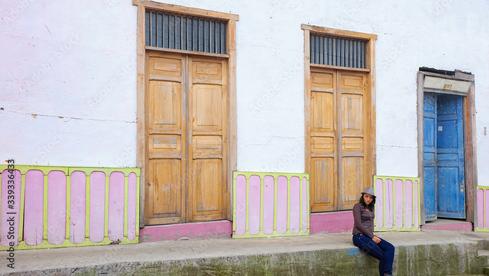 Woman with hat sitting on the sidewalk in front of an old house in the city of Salento, Quindio, Colombia