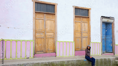 Obraz na płótnie Woman with hat sitting on the sidewalk in front of an old house in the city of Salento, Quindio, Colombia w salonie