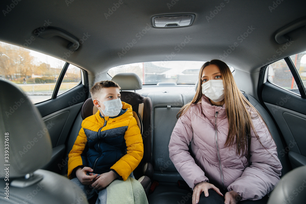 A mother with a child in the back seat of a car in masks going to the hospital. Epidemic, quarantine