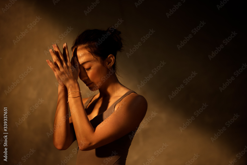 Young Asian woman practicing yoga in moody studio during golden hour