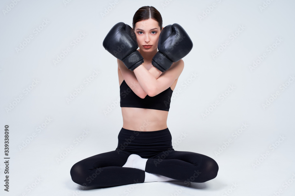 A young woman in black boxing gloves sits on a white background.