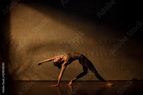 Young Asian woman practicing yoga in moody studio during golden hour photo