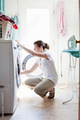 Candid picture of woman keeping things clean, doing laundry at home, folding clothes from a hamper, placing clothes in washing machine 