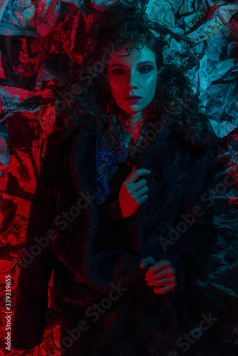 haute couture with pink blue neon hair. Young beautiful woman model, fashionable glowing hairstyle, makeup. Stylish Art Studio Portrait. Colorful Bright Light. black coat, newspaper background