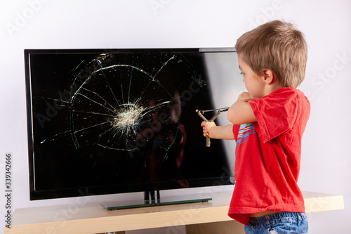 Foto Cute small boy aiming to shattered TV screen with a slingshot.