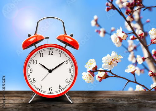 Vintage red alarm clock on wooden table or bench in the spring season on the background of a blooming fruit tree background.