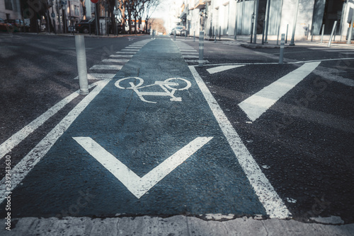 Wide-angle view of a modern urban road with bicycle marking sign on a bluish asphalt and a pedestrian crossing in a distance, plastic posts in the foreground, Lisbon, Portugal