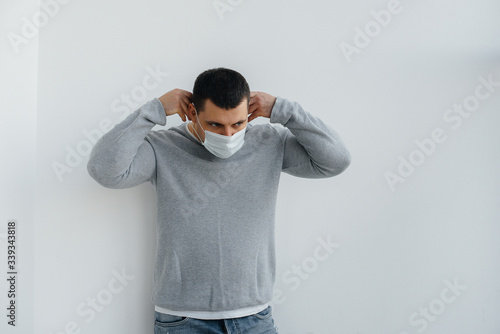 A young man stands on a gray background wearing a mask during a quarantine with free space. Quarantine in the mask