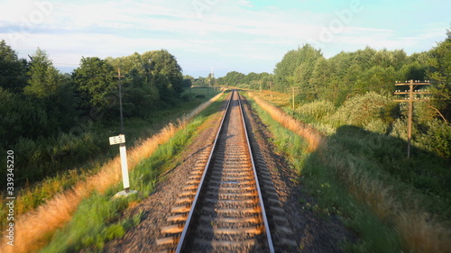 Fototapeta Naklejka Na Ścianę i Meble -  Back view of railroad and a beautiful green nature from a train passing on countryside land. Railroad travel or railway tourism concept. Slow motion back view 4K video.