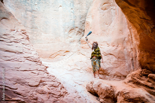 Distant caveman standing outdoors in a cave waving his club in the air in triumph