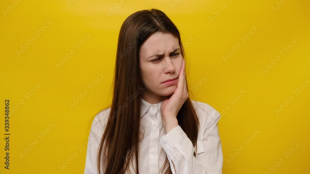 Tired woman touch cheek, suffers from toothache, unhappy girl having terrible sudden tooth pain, need dental treatment, wears shirt, isolated on yellow studio background. Medical insurance concept Tired woman touch cheek, suffers from toothache, unhappy girl having terrible sudden tooth pain, need dental treatment, wears shirt, isolated on yellow studio background. Medical insurance concept