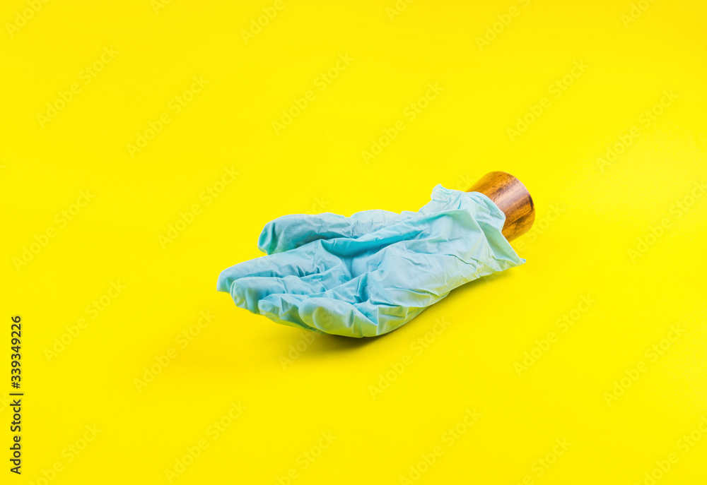 Palm of wooden hand wearing blue medical glove on yellow bold color paper background. Art creative concept in times of Coronavirus covid19 pandemic Palm of wooden hand wearing blue medical glove on yellow bold color paper background. Art creative concept in times of Coronavirus covid19 pandemic