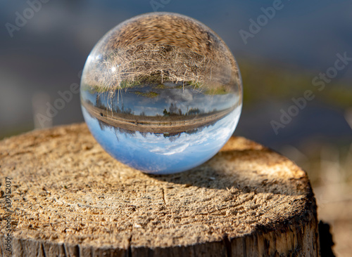 Inverted image of the river and its banks in a glass ball standing on a stump. Selective focus. Early spring landscape.