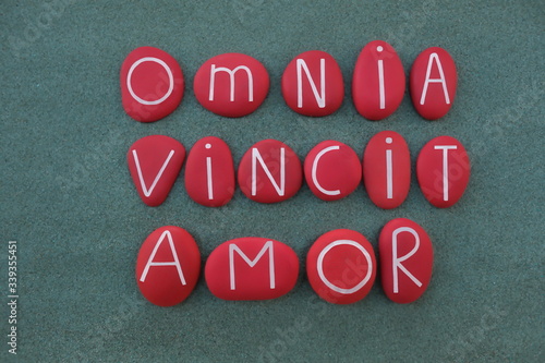 Omnia Vincit Amor, Love conquers all, latin famous, Virgil, text composed with red colored stone letters over green sand photo