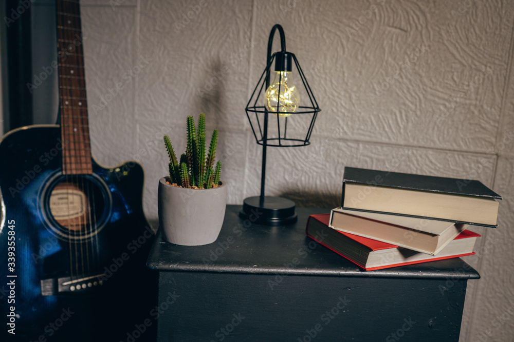 Obraz premium detail of the corner of a comfortable room with guitar, books, cloth stool, plant and a lamp