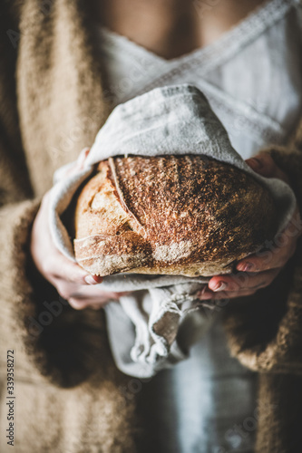 Woman holding freshly baked healthy rye Swedish bread round loaf in hands, selective focus