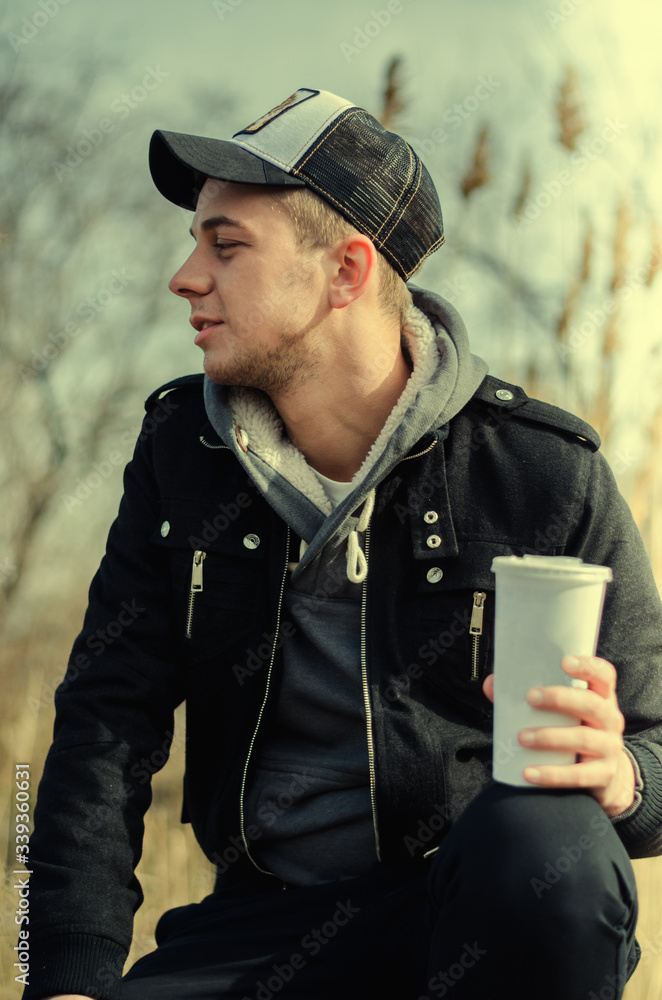 Portrait of a young guy sitting by the river with a glass of drink Portrait of a young guy sitting by the river with a glass of drink