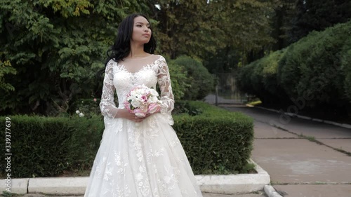 pretty woman wearing gorgeous long lacy wedding dress with small bouquet poses in green park slow motion photo