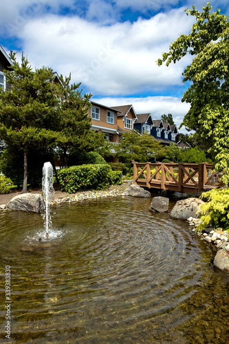 Residential District in Richmond City, a village of townhouses with pond and fountain, green grass bushes and trees in the territory of residential complex, Vancouver, British Columbia, Canada