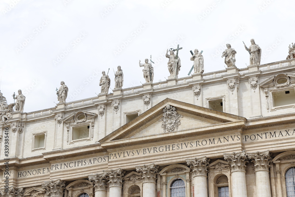Statues of Christ and the Apostles and Oltramontano Clock on top of the facade of St Peter's Basilica with blue sky and clouds in Vatican City