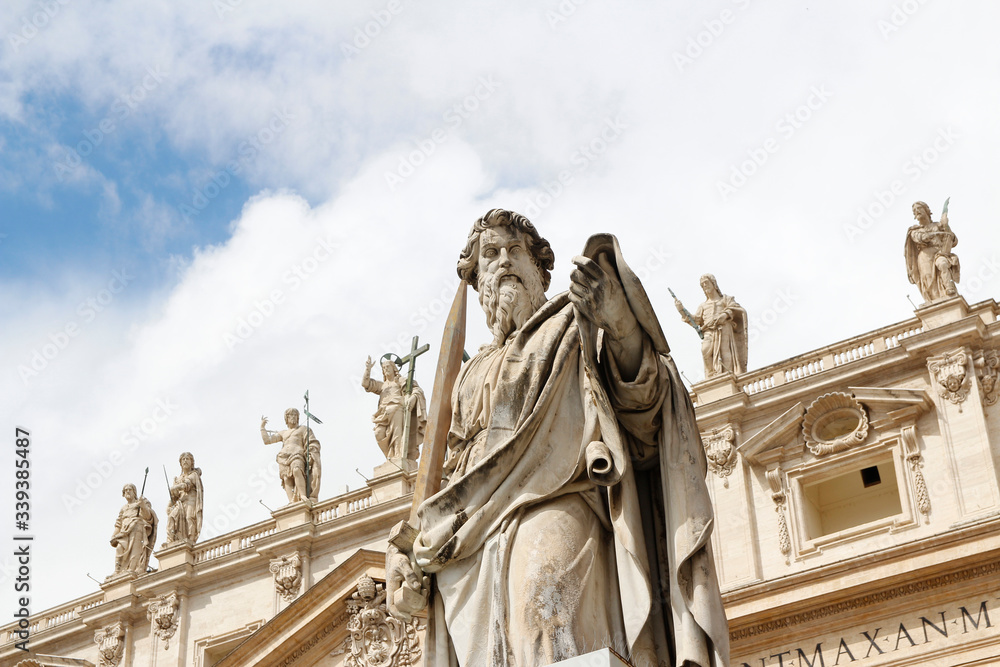 Statue of St. Paul with sword in front of St Peter's Basilica with blue sky and clouds in Vatican City, Rome, Italy