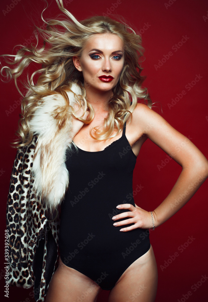 Beautiful fashionable woman with blond hair, dressed in a leopard jacket, holds a bag and poses on a red background. Beautiful fashionable woman with blond hair, dressed in a leopard jacket, holds a bag and poses on a red background.