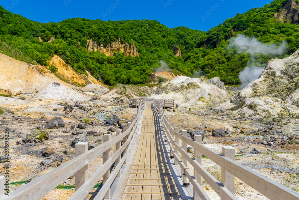 View of wooden pathway for sightseeing in Jigokudani valley or hell valley and blue sky background in summer. Natural Landscape and active volcano in Noboribetsu, Hokkaido, North of Japan.