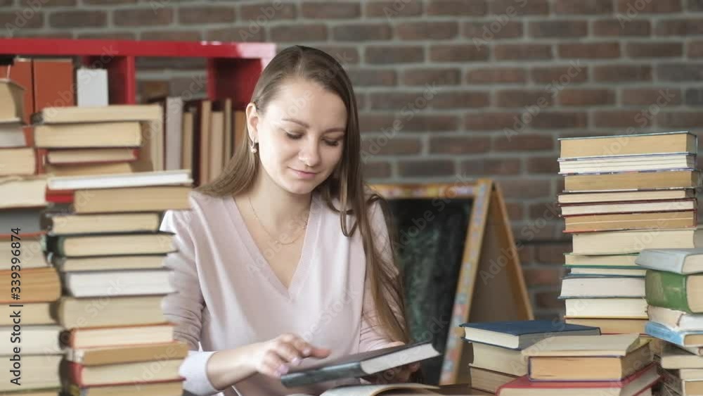 beautiful young girl is sitting in room home table and reading book. student studies home. Exam preparation. woman reads textbook among a lot of books. home education. The concept of modern education. beautiful young girl is sitting in room home table and reading book. student studies home. Exam preparation. woman reads textbook among a lot of books. home education. The concept of modern education.