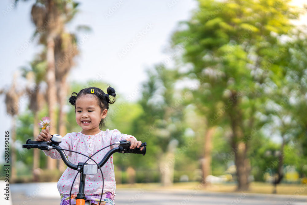 Cute asian girl wearing long sleeved pink shirt
cycling on her bike at village.