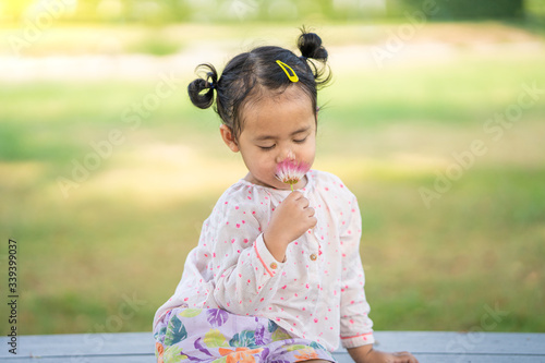 Cute little girl with pink shirt holding tropical pink flower at garden.