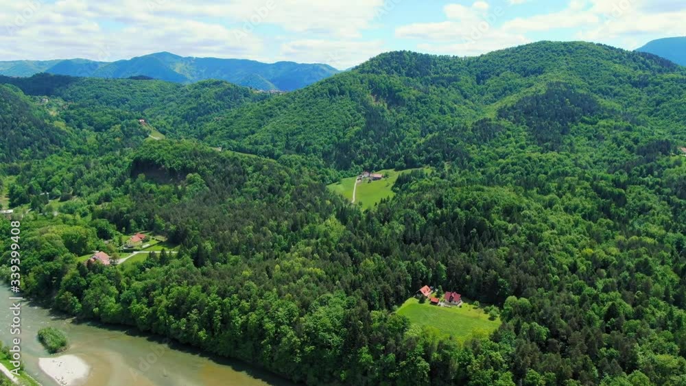 Isolated houses in the glades of a dense forest in a colorful mountain landscape behind a river. Drone aerial shot. Isolated houses in the glades of a dense forest in a colorful mountain landscape behind a river. Drone aerial shot.