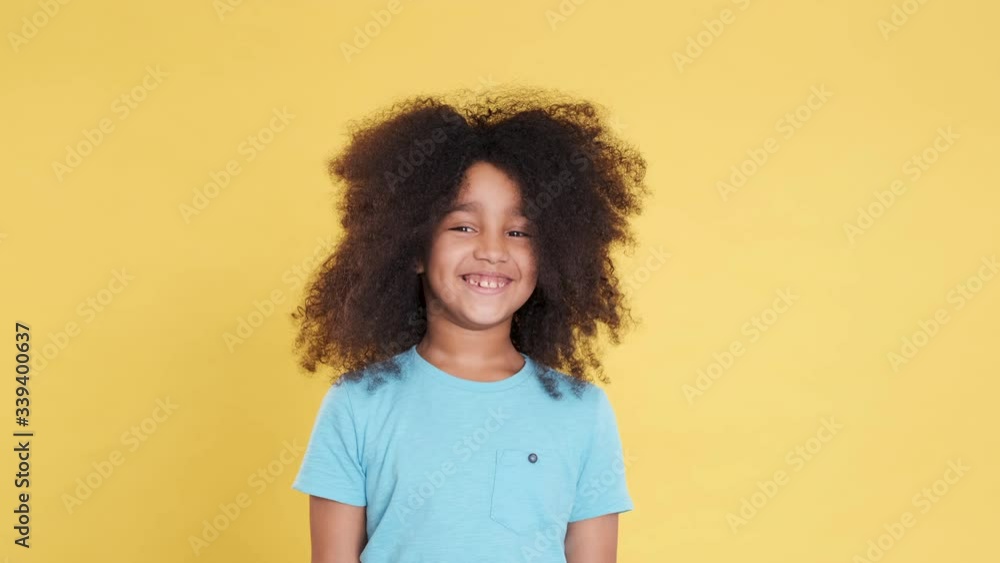 Smiling and Looking in Camera. Pleasant Dark-Skinned African American Little Girl Shows Happiness, Joyful, Good Emotions. Lush Curly Hair, Concept of Positive Thinking, Active Lifestyle. Slow motion. Smiling and Looking in Camera. Pleasant Dark-Skinned African American Little Girl Shows Happiness, Joyful, Good Emotions. Lush Curly Hair, Concept of Positive Thinking, Active Lifestyle. Slow motion.