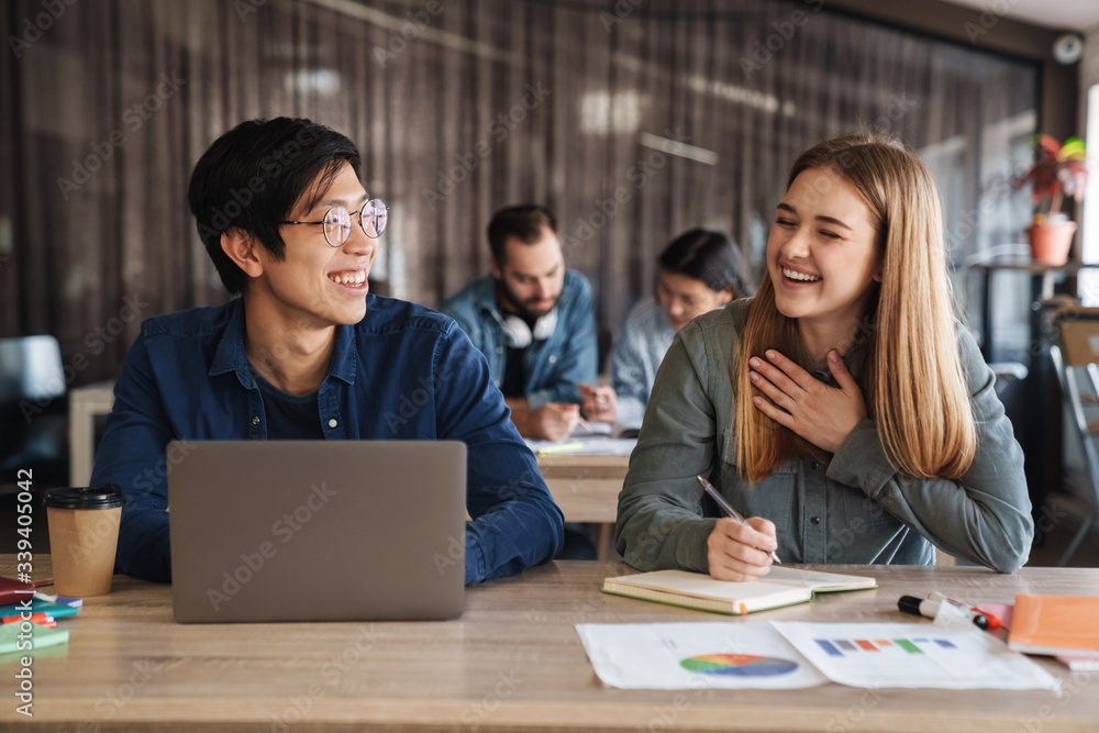 Photo of laughing students using laptop and writing in exercise book Photo of laughing students using laptop and writing in exercise book