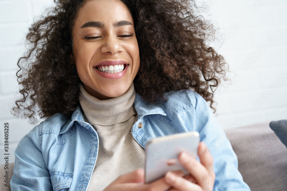 Cheerful afro american young woman hold smart phone using app, video  calling, watching funny videos in