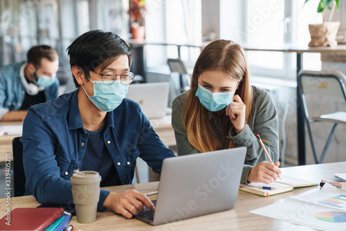 Image of students in protective mask talking while studying with laptop