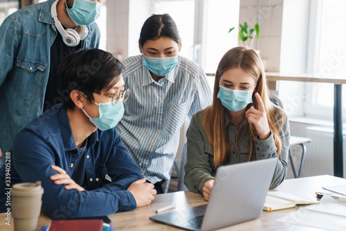 Image of students in protective mask talking while studying with laptop