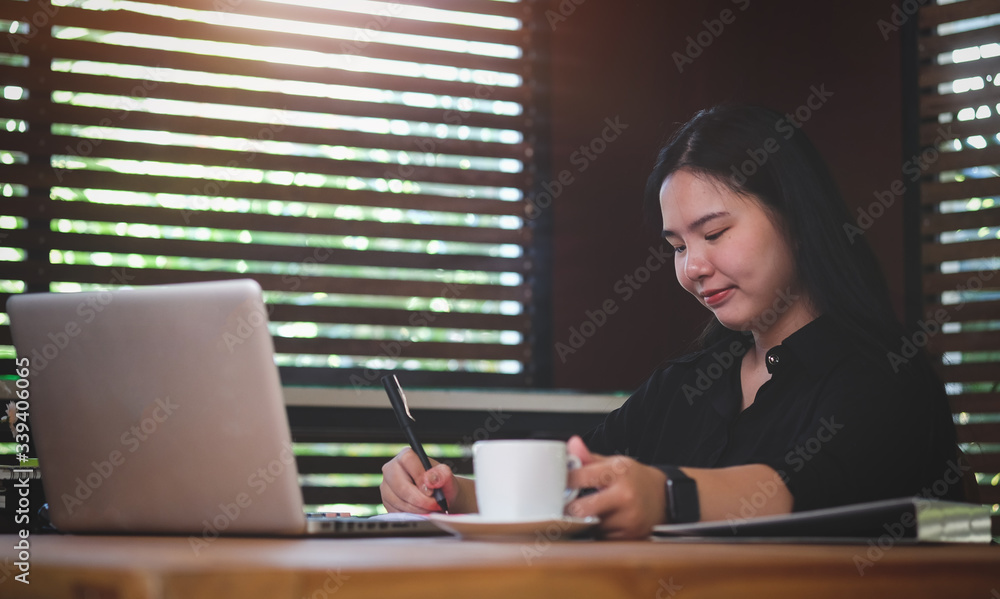 Woman working from home on laptop computer while sitting at the living room, drinking coffee