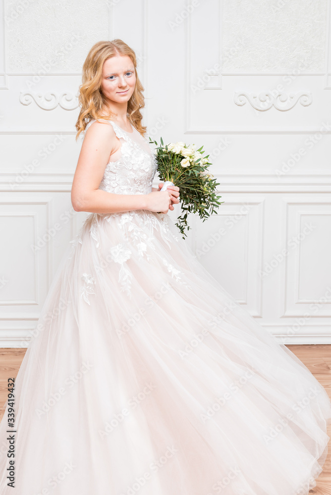 Romantic young bride in elegant hotel room in white lace wedding dress with makeup and wavy blonde hair with wedding bouquet in her hands getting ready in bride's morning. Fine art wedding. Romantic young bride in elegant hotel room in white lace wedding dress with makeup and wavy blonde hair with wedding bouquet in her hands getting ready in bride's morning. Fine art wedding.
