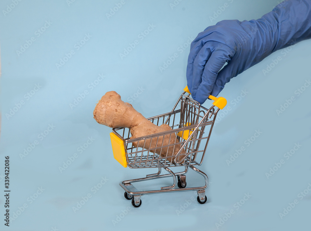 Female hand in a blue rubber glove rolls a supermarket cart with ginger on a blue background. Spice. Protection. Covid 19