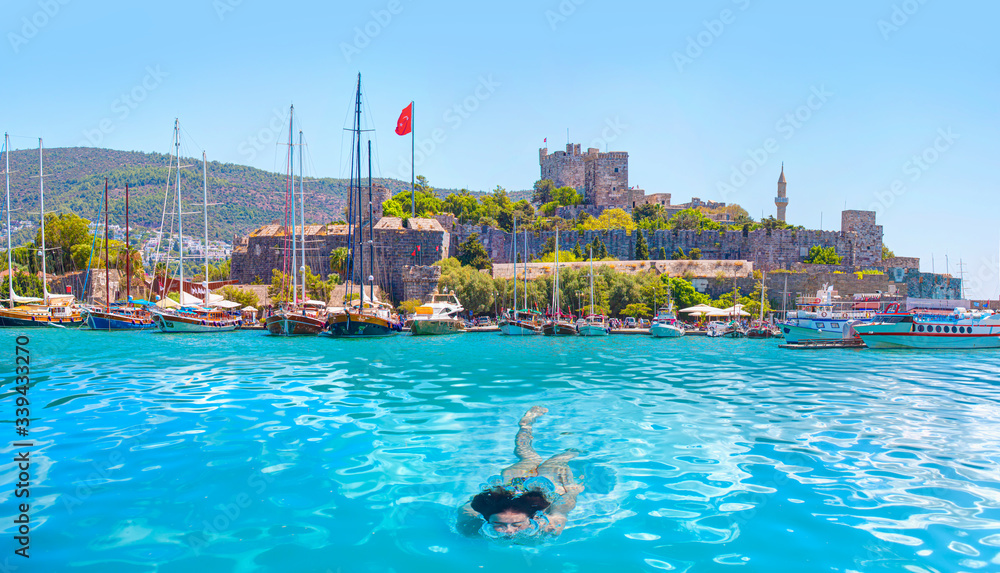 Young girl swimming in the sea with Panoramic view of Saint Peter Castle (Bodrum castle) and marina - Bodrum, Turkey