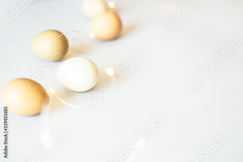 Stylish Easter holiday eggs of natural color on a light background with lights, lanterns and garlands. Flat lay