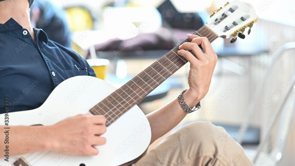Fototapeta premium Cropped image of smart man relaxing by playing an acoustic guitar while sitting at the modern chair over comfortable sitting room as background.