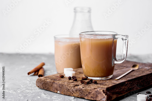 Cooled coffee with milk, cinnamon sticks, coffee beans, sugar, spoon on the table.