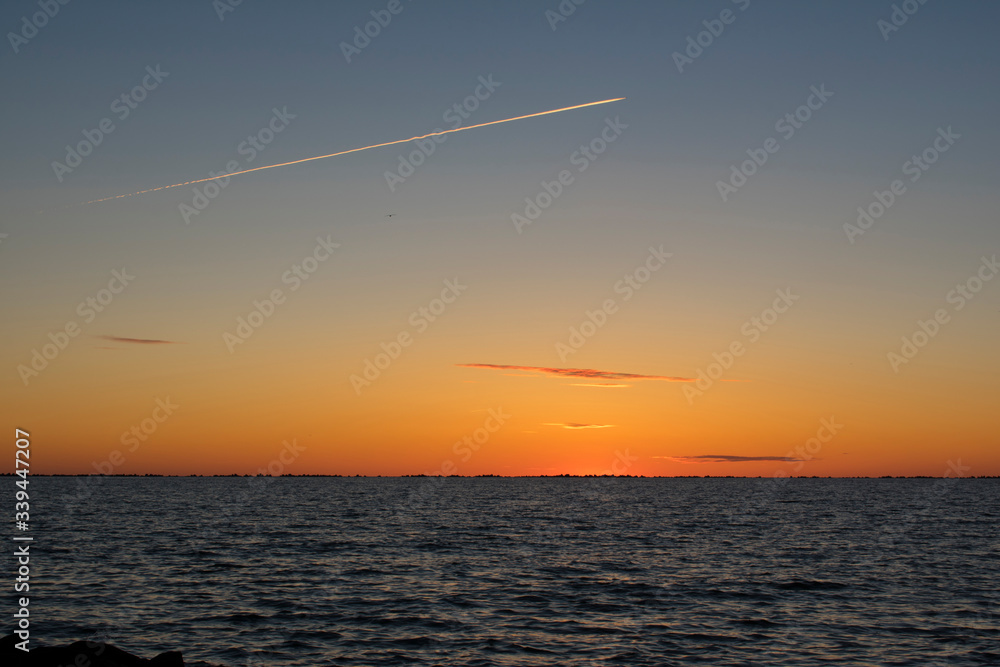 Beautiful orange sunset at sea with airplane chemtrail over sky Beautiful orange sunset at sea with airplane chemtrail over sky