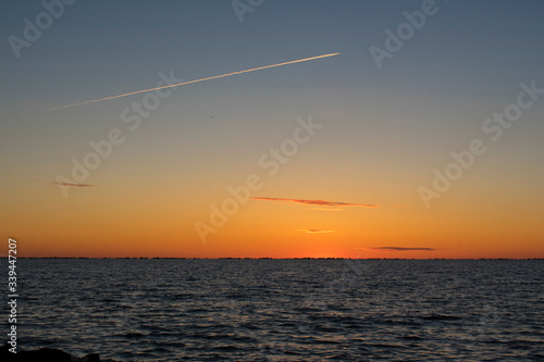 Beautiful orange sunset at sea with airplane chemtrail over sky